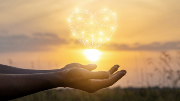 Hands holding a glowing heart of light at sunset